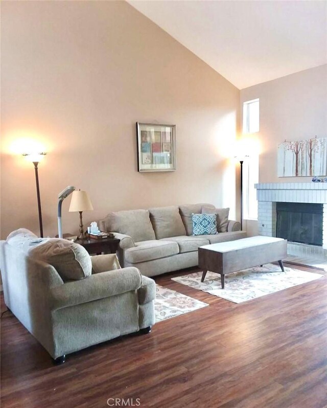 living room with a brick fireplace, dark hardwood / wood-style flooring, and high vaulted ceiling