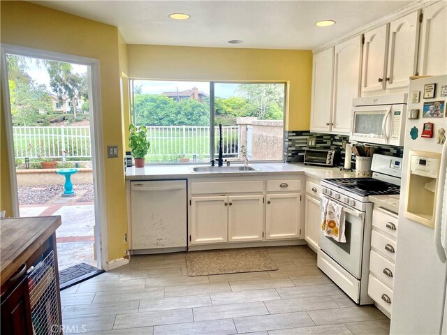 kitchen with white cabinetry, sink, decorative backsplash, and white appliances