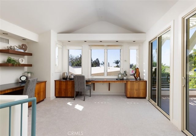 office area featuring vaulted ceiling, built in desk, light carpet, and a healthy amount of sunlight