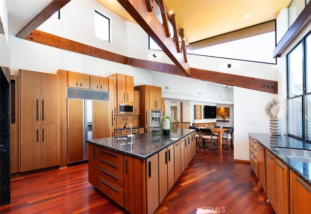 kitchen with dark wood-style floors, dark stone counters, a sink, and built in appliances