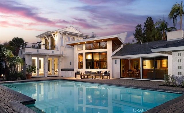 back of house at dusk with a patio, a balcony, an outdoor hangout area, french doors, and an outdoor pool