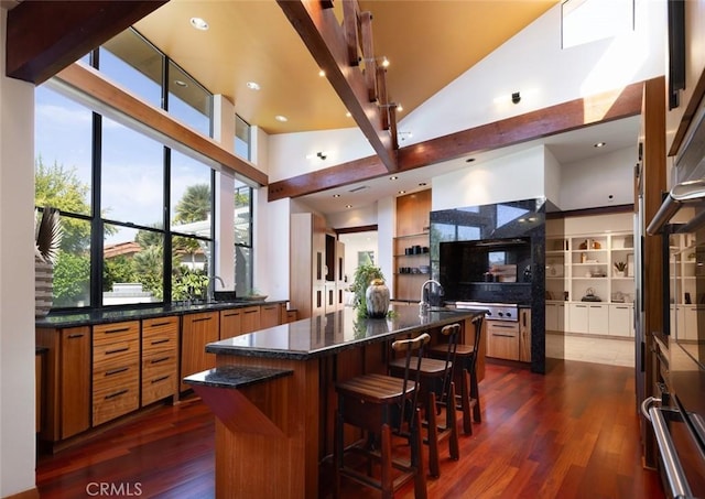 kitchen with a breakfast bar, dark wood-style flooring, brown cabinets, dark stone countertops, and a large island with sink