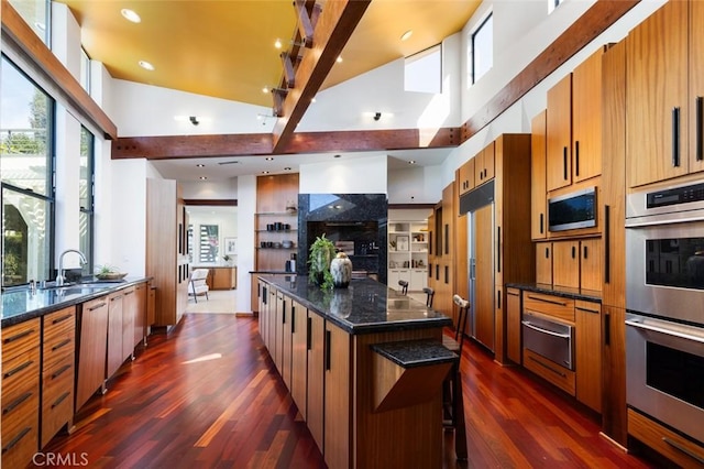 kitchen featuring dark wood-style floors, a kitchen island, built in appliances, a sink, and a warming drawer