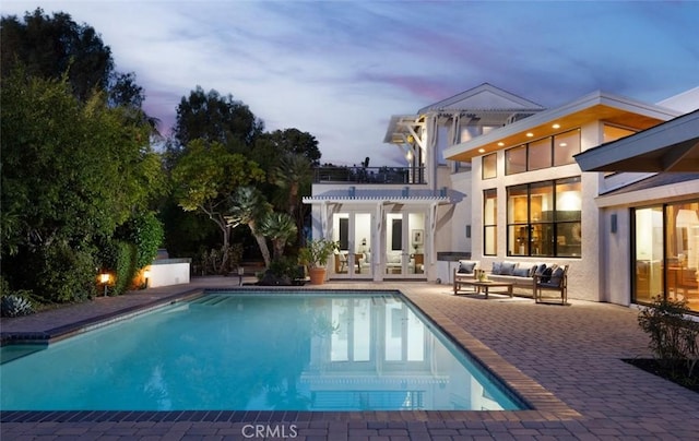 pool at dusk featuring a patio area and outdoor lounge area