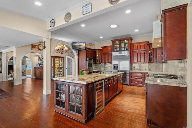 kitchen with sink, an island with sink, beverage cooler, backsplash, and appliances with stainless steel finishes