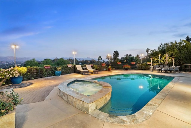 pool at dusk featuring a patio area, an in ground hot tub, and a mountain view