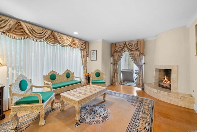 sitting room with a tiled fireplace, ornamental molding, and hardwood / wood-style flooring