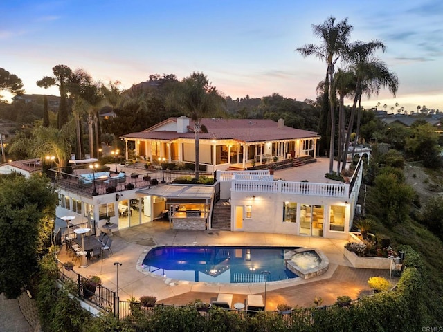 pool at dusk with a patio and an in ground hot tub