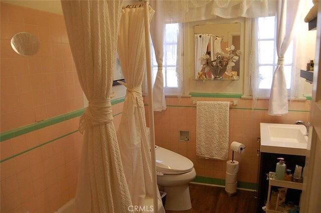 bathroom with wood-type flooring, tile walls, toilet, and a wealth of natural light