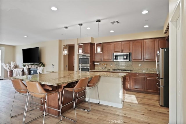 kitchen with stainless steel appliances, a spacious island, a breakfast bar area, decorative backsplash, and pendant lighting