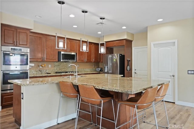 kitchen featuring a large island, light stone counters, hanging light fixtures, and appliances with stainless steel finishes