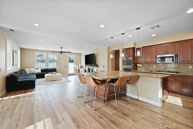 kitchen featuring stainless steel appliances, decorative light fixtures, ceiling fan, a breakfast bar area, and backsplash