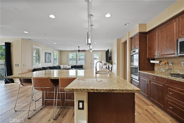 kitchen featuring appliances with stainless steel finishes, a large island with sink, a kitchen bar, sink, and decorative light fixtures