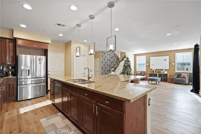 kitchen with stainless steel appliances, sink, decorative light fixtures, light hardwood / wood-style floors, and a kitchen island with sink