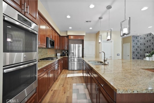 kitchen featuring light stone counters, decorative light fixtures, stainless steel appliances, backsplash, and sink