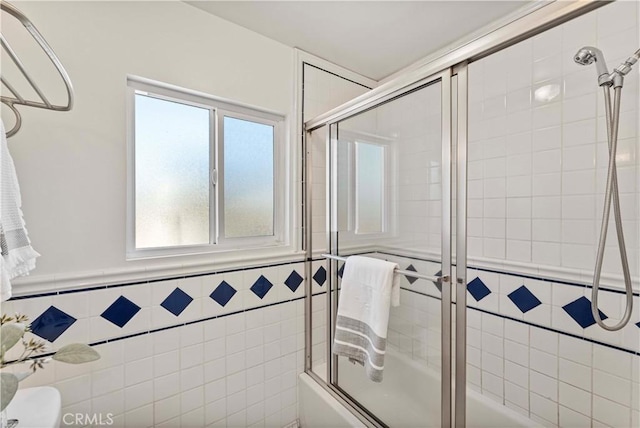 bathroom with toilet, tile walls, and bath / shower combo with glass door