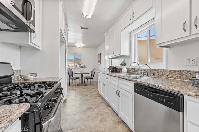 kitchen with light stone countertops, a wealth of natural light, stainless steel appliances, white cabinetry, and sink