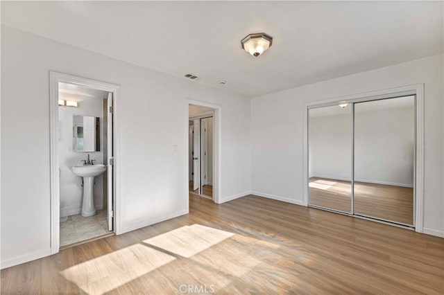 unfurnished bedroom featuring hardwood / wood-style floors, a closet, and ensuite bath