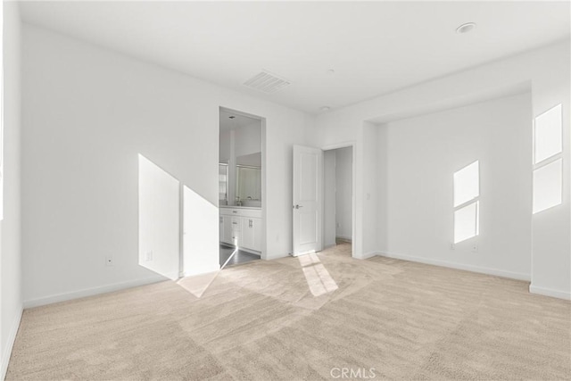 unfurnished bedroom with baseboards, light colored carpet, visible vents, and ensuite bath