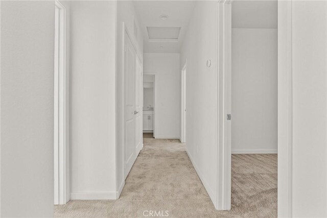 corridor with attic access, baseboards, and light colored carpet