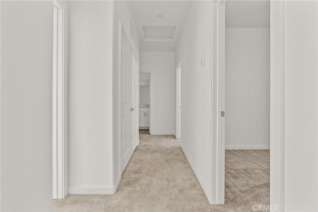 corridor with baseboards, light carpet, and attic access