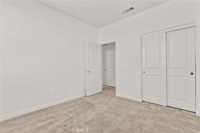 unfurnished bedroom featuring baseboards, visible vents, a closet, and light colored carpet