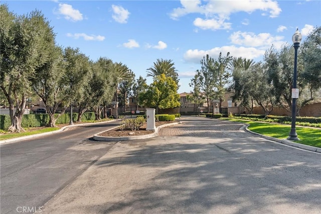 view of street featuring sidewalks, curbs, a gated entry, and street lights