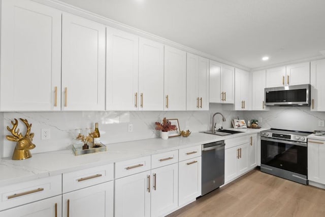 kitchen with decorative backsplash, white cabinets, light hardwood / wood-style flooring, and stainless steel appliances