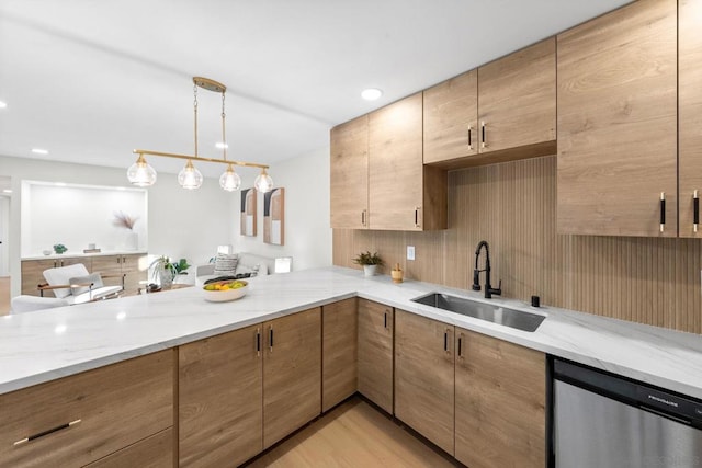 kitchen with light stone counters, stainless steel dishwasher, pendant lighting, and sink