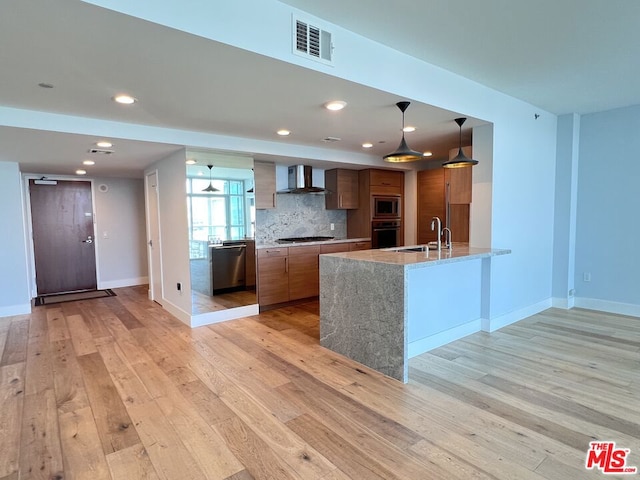 kitchen featuring light stone countertops, appliances with stainless steel finishes, wall chimney range hood, sink, and hanging light fixtures