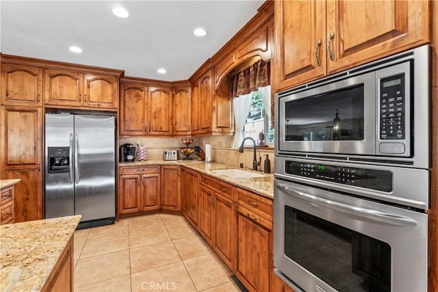 kitchen with light stone countertops, light tile patterned floors, appliances with stainless steel finishes, and sink