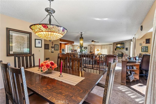 carpeted dining area featuring ceiling fan, a brick fireplace, and a textured ceiling