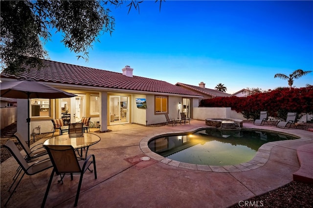 pool at dusk with an in ground hot tub and a patio area