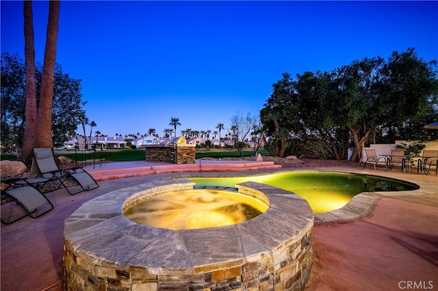 pool at dusk with an in ground hot tub and a patio area