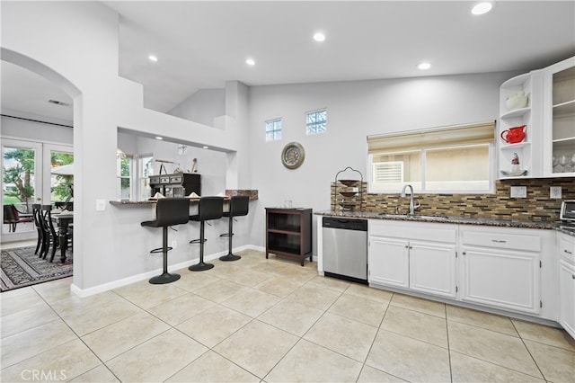 kitchen featuring dark stone countertops, lofted ceiling, white cabinets, stainless steel dishwasher, and backsplash