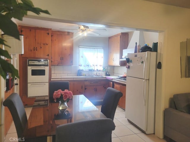 kitchen featuring light tile patterned floors, ceiling fan, backsplash, white appliances, and sink