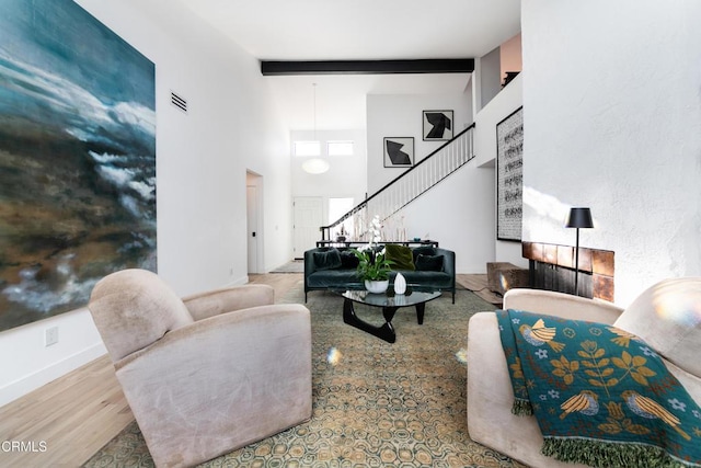 living room featuring beamed ceiling, a high ceiling, and light hardwood / wood-style flooring