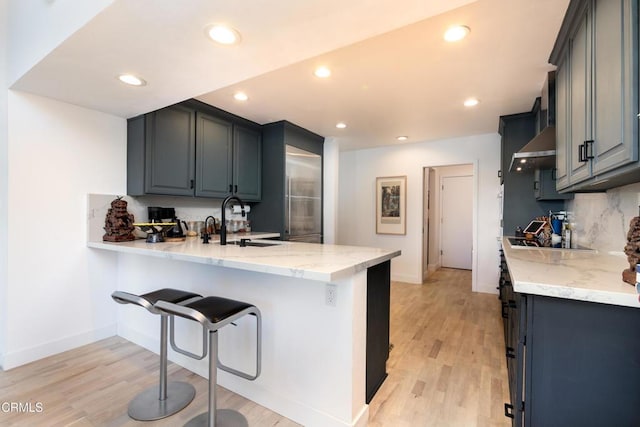 kitchen featuring recessed lighting, light wood-style flooring, a sink, wall chimney range hood, and a peninsula