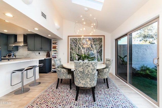 dining area featuring a chandelier, vaulted ceiling with skylight, light wood-type flooring, and visible vents