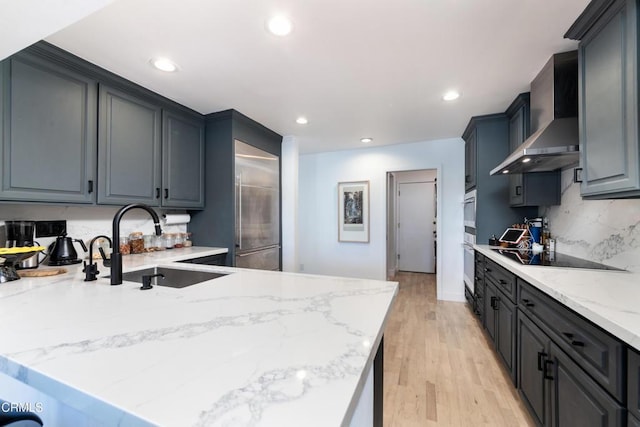 kitchen with decorative backsplash, a sink, wall chimney range hood, a peninsula, and black electric cooktop