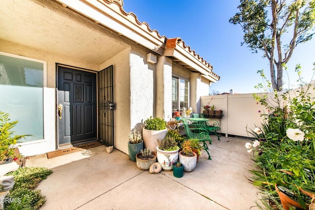 doorway to property with a patio area, a tiled roof, fence, and stucco siding