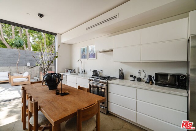 kitchen featuring stainless steel gas stove, light stone counters, concrete flooring, white cabinets, and sink