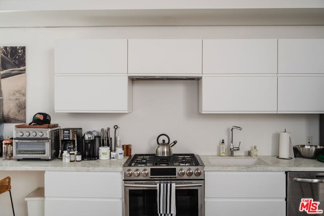 kitchen featuring light stone counters, stainless steel appliances, white cabinetry, and sink