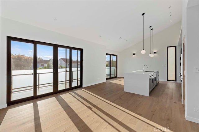 kitchen with sink, decorative light fixtures, wood-type flooring, high vaulted ceiling, and a kitchen island with sink