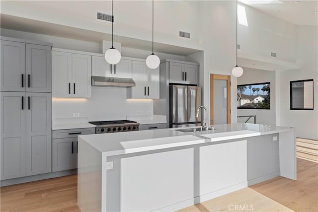 kitchen featuring a center island with sink, decorative light fixtures, gray cabinetry, and stainless steel fridge