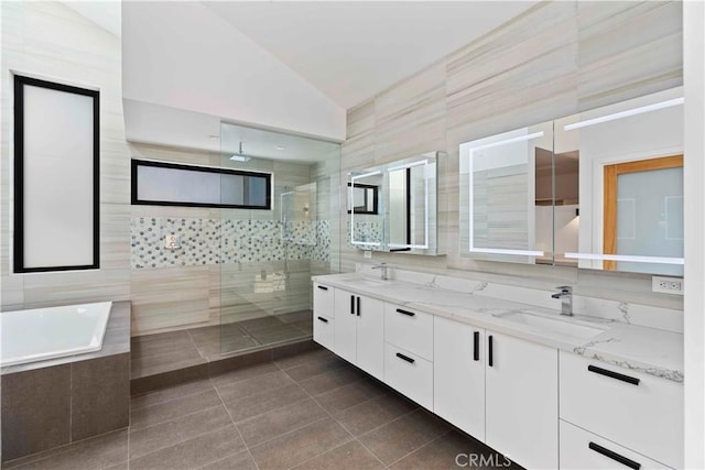 bathroom with tile patterned flooring, vaulted ceiling, plus walk in shower, vanity, and tile walls