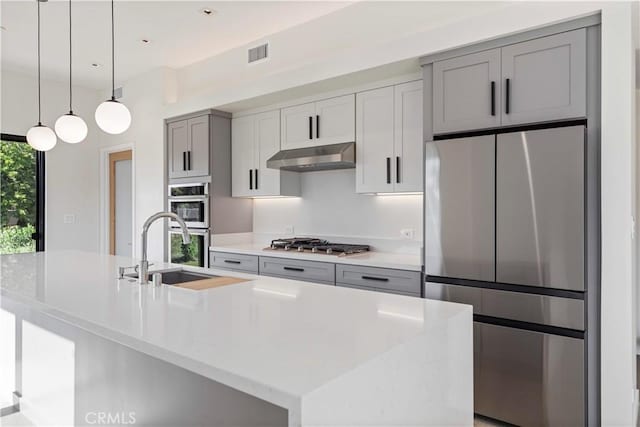 kitchen with decorative light fixtures, stainless steel appliances, a center island with sink, gray cabinets, and sink