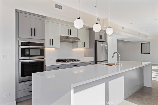 kitchen featuring decorative light fixtures, stainless steel appliances, a center island with sink, gray cabinetry, and sink