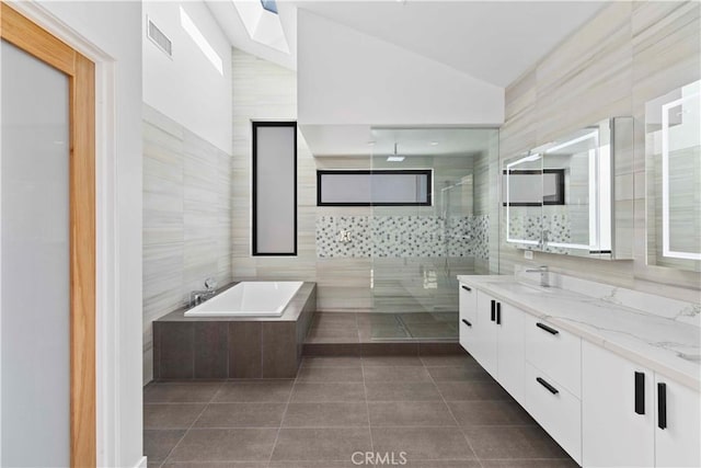 bathroom with vaulted ceiling, tile walls, tile patterned floors, independent shower and bath, and vanity