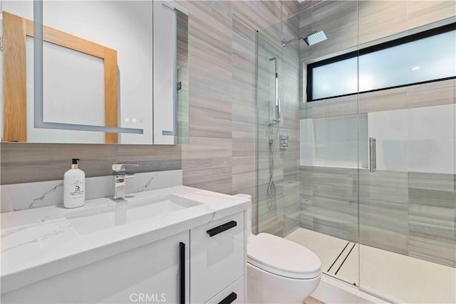 bathroom featuring toilet, tile walls, a shower with door, backsplash, and vanity